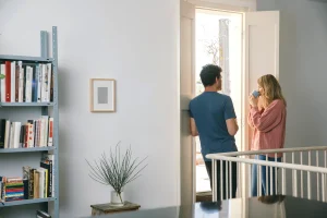 a male and a female standing by a window talking and drinking coffee
